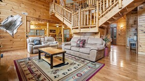 A log cabin interior with a wooden staircase, two sofas, a coffee table, and a rug. - 5BR Cabin w Yard Office Hot Tub Firepit (Sevierville)
