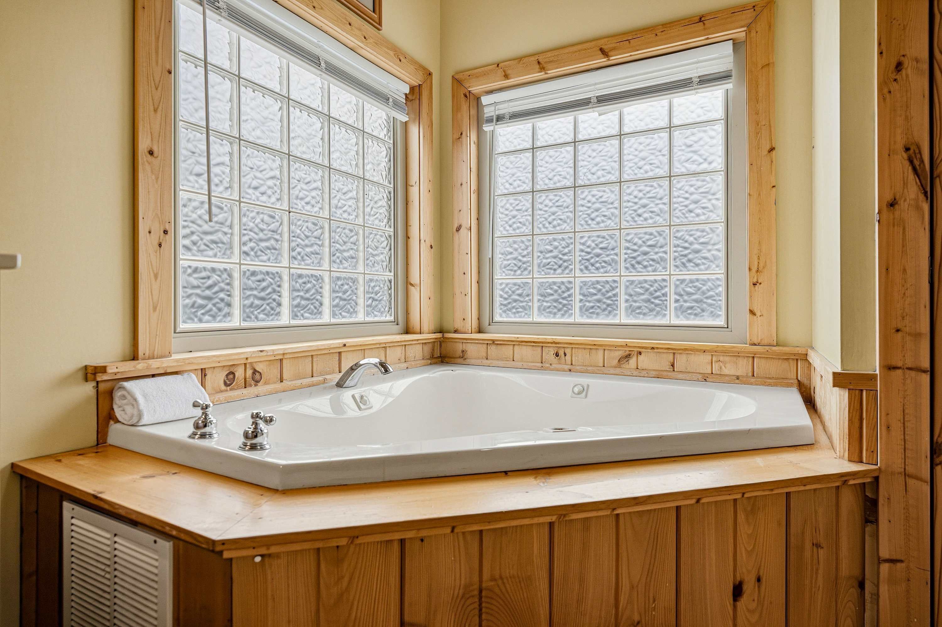 A bathroom with a freestanding bathtub, wooden paneling, and frosted glass windows.