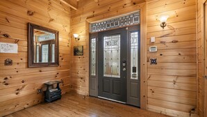 A wooden interior with a dark wooden door, a mirror, a small table with a basket, and a light fixture above the door. - 5BR Cabin w Yard Office Hot Tub Firepit (Sevierville)