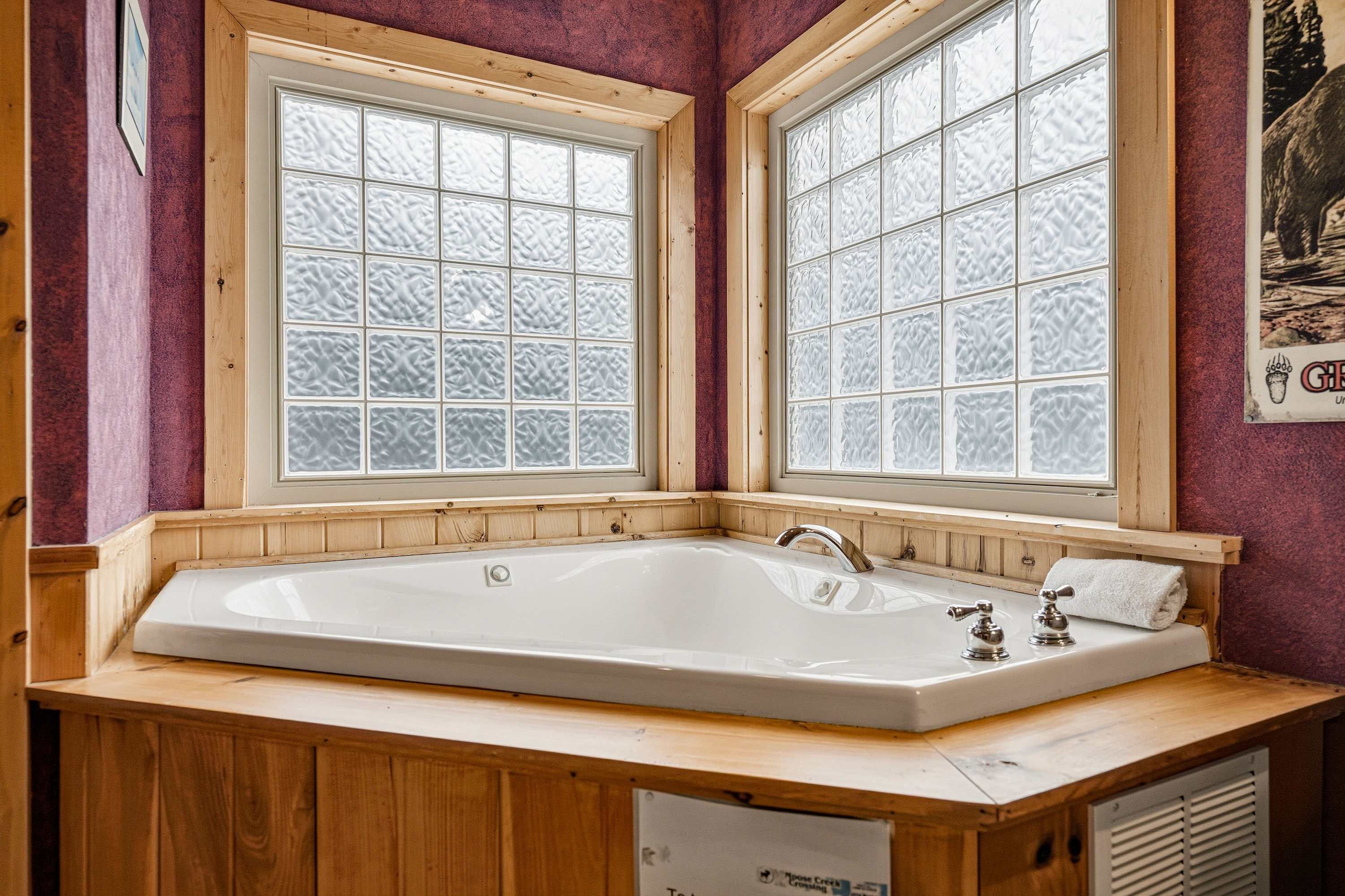 Un baño con una bañera grande, tocador de madera, ventanas con vidrio esmerilado y un cartel en la pared.