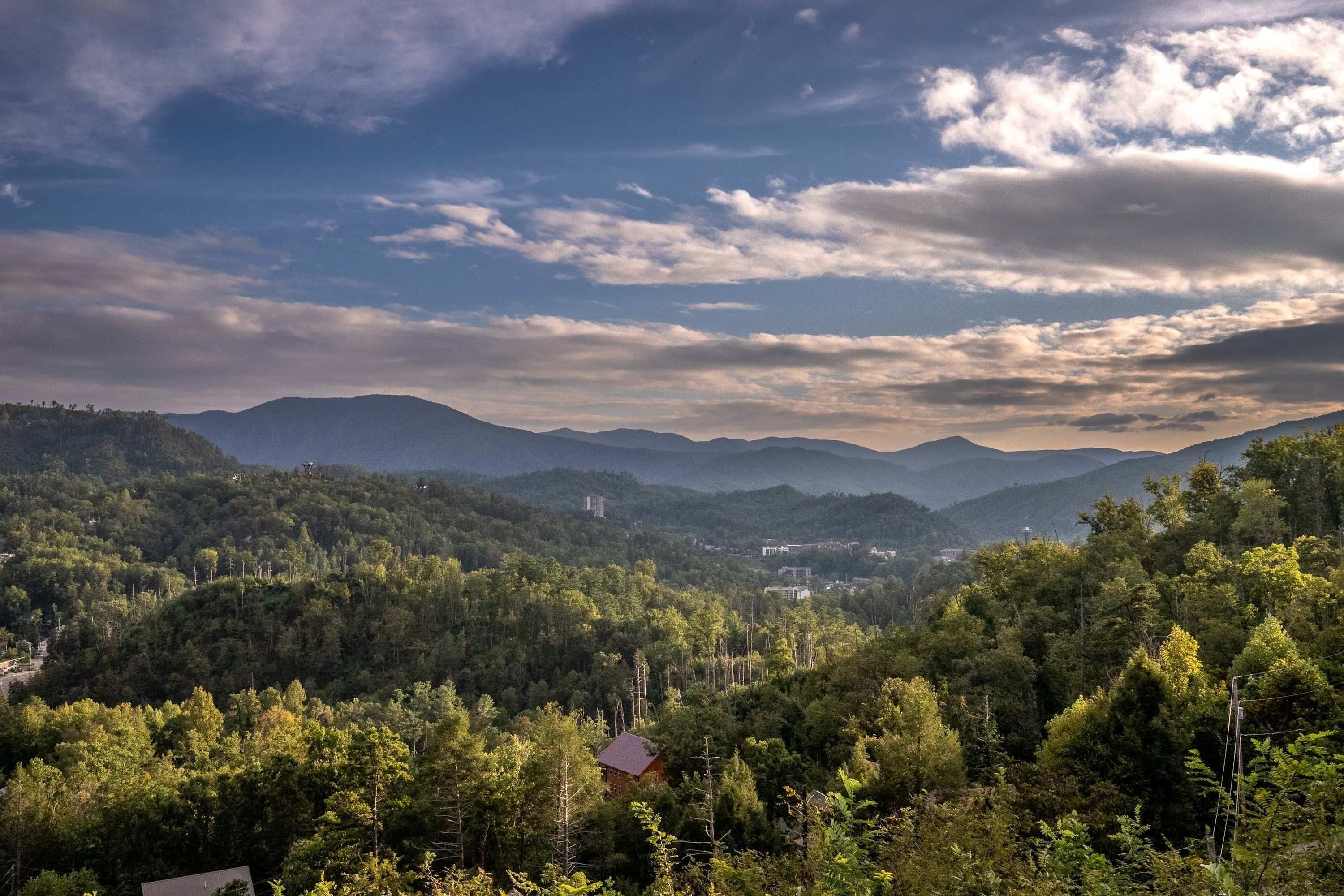 Un paysage montagneux avec une forêt dense et un petit bâtiment au premier plan.