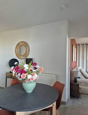Un coin repas comprenant une table ronde, des chaises, un vase de fleurs, un miroir fixé au mur et un radiateur.