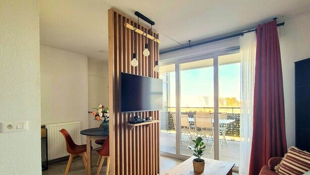 Een moderne woonkamer met een flatscreen televisie, een eethoek met rode stoelen, een houten salontafel en een bank.