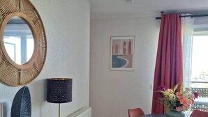 Een moderne eetruimte met een ronde tafel, rode stoelen, een houten buffetkast, een wandspiegel en een lijstwerk met kunst.