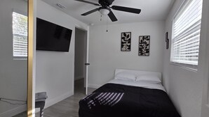 Une chambre à coucher comprenant un lit, un ventilateur de plafond, un téléviseur fixé au mur et deux œuvres d’art encadrées.
