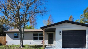 Une maison de plain-pied avec un garage à l’avant, un petit porche et un arbre dans la cour.