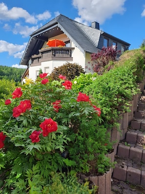 Ein Haus mit schrägem Dach, einem Balkon und einem Garten mit roten Blumen.