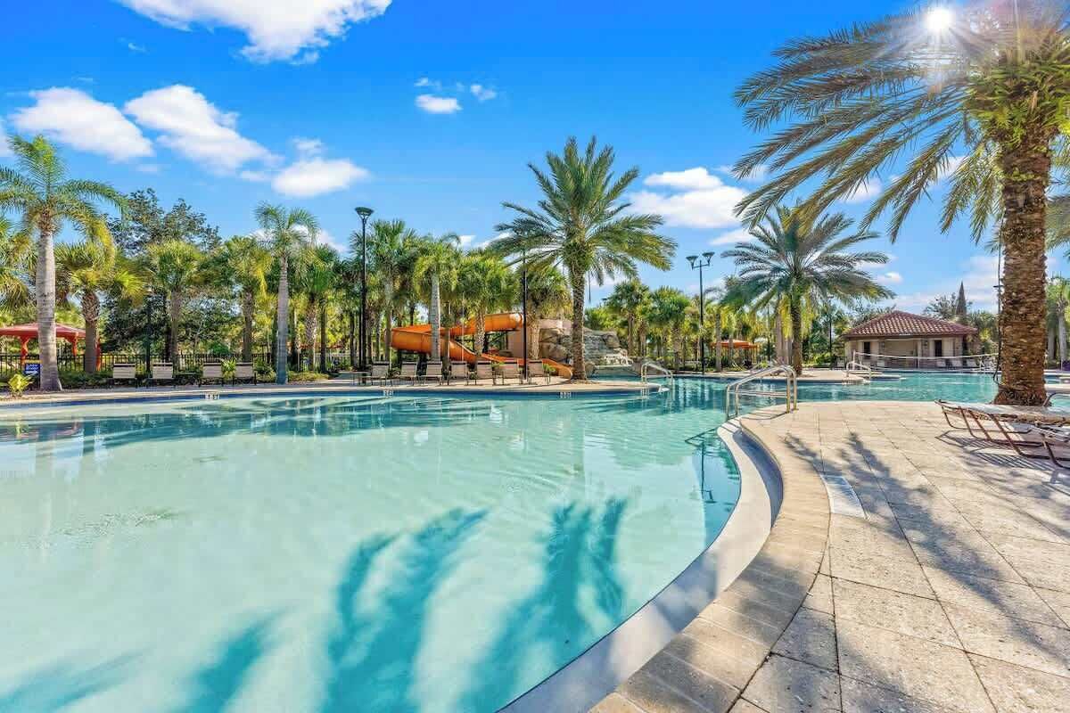 A pool area with a water slide, palm trees, and a small building.