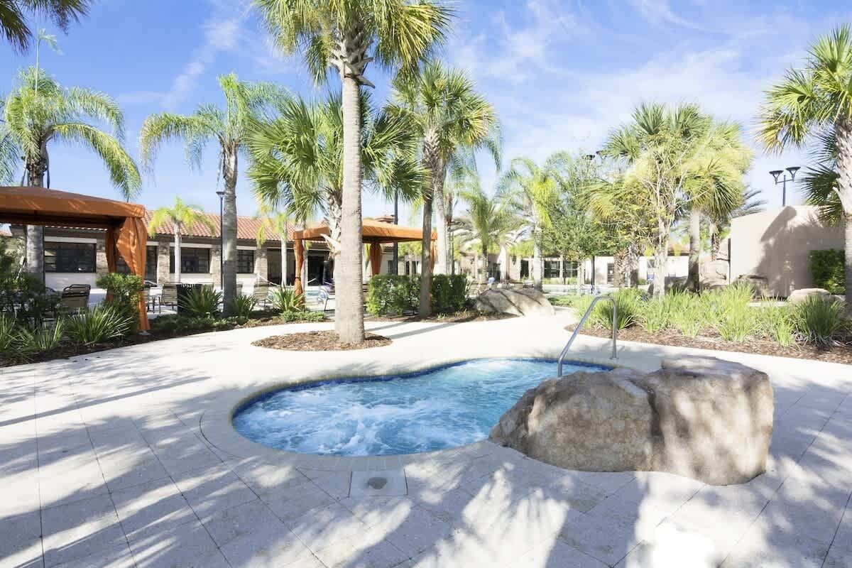 A pool area with palm trees, a hot tub, and a stone feature.