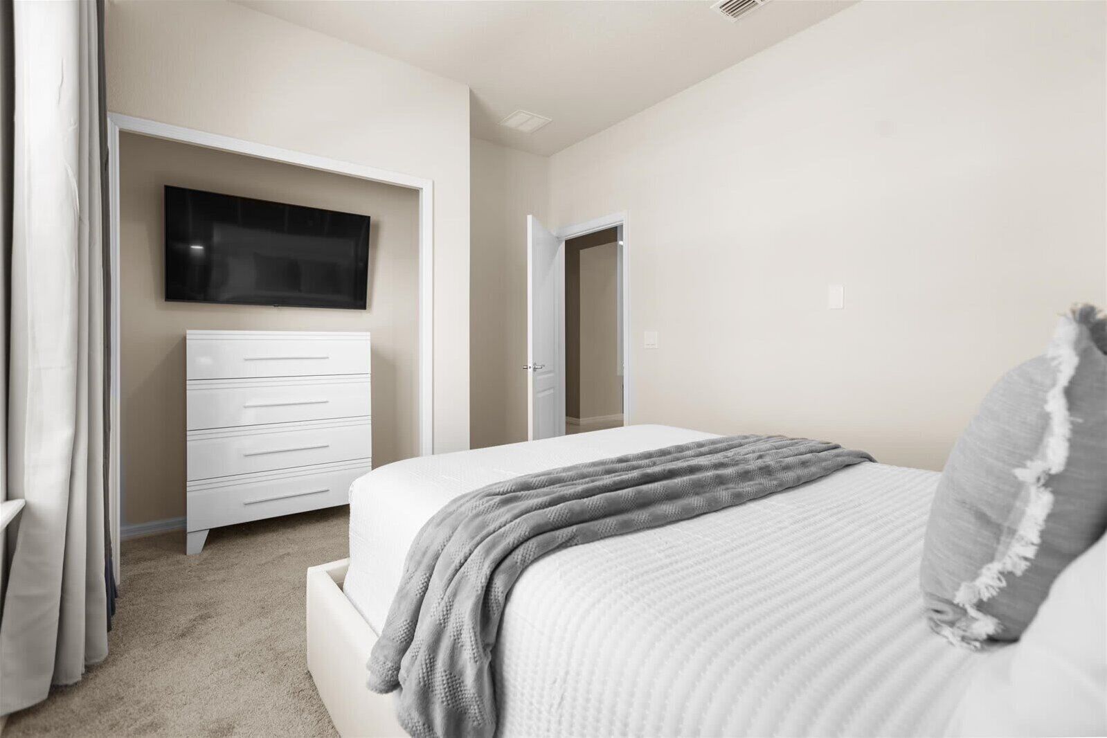 Ein Schlafzimmer mit Bett, Kommode, Fernseher und einer Tür.