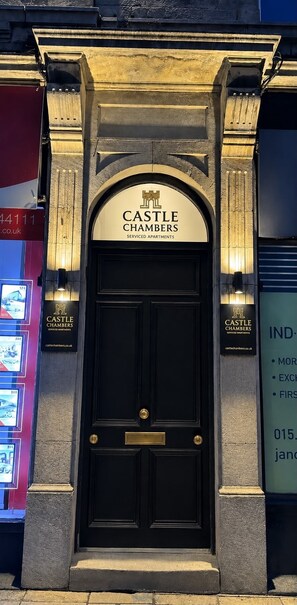 Une porte noire à deux battants, sur laquelle on peut lire l’inscription « CASTLE CHAMBERS » et « APPARTEMENTS AVEC SERVICES ».