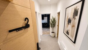 En gang med en trædør mærket 'Castle Chambers', en potteplante og et rammet abstrakt maleri på væggen.