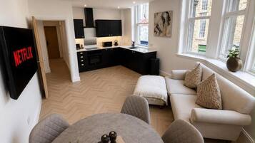 Een moderne woonkamer met een bank, een eettafel met stoelen, een keuken en een aan de muur bevestigde televisie.