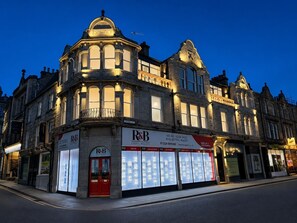 Un bâtiment historique, reconnaissable à son enseigne imposante d'une agence immobilière spécialisée dans la musique R&B, à ses grandes vitrines et à son style architectural classique.