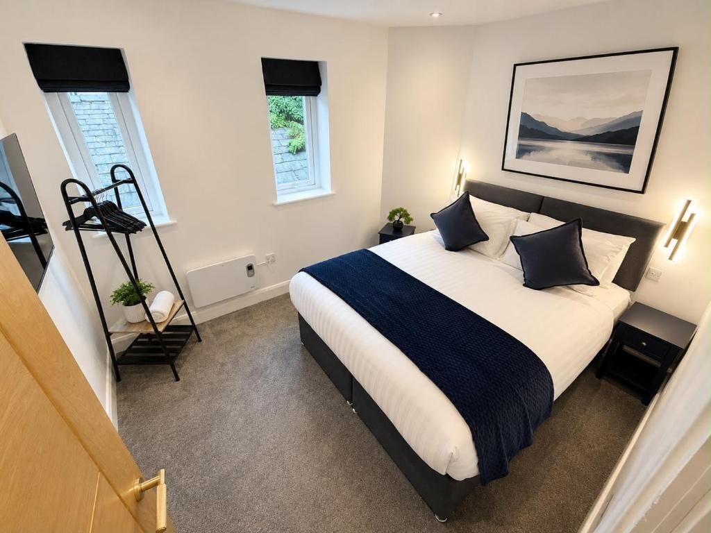 A bedroom with a bed, bedside tables, a window, a wall-mounted picture, and a coat rack.