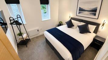 A bedroom with a bed, bedside tables, a window, a wall-mounted picture, and a coat rack.