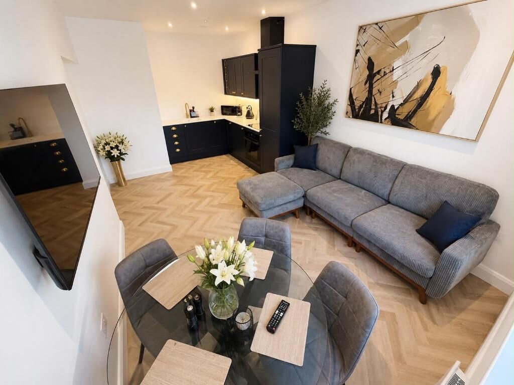 A modern living room with a gray sectional sofa, a glass coffee table, and a dining area with a small table and chairs.