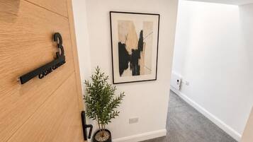 A hallway with a wooden door labeled '3', a framed abstract painting, and a potted plant.