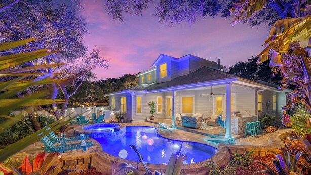 Una casa a due piani con piscina, area salotto esterna e patio ben illuminato.