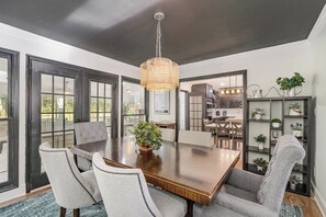 Un comedor con una gran mesa de madera, cuatro sillas tapizadas de color gris, una lámpara colgante de mimbre y una planta en maceta sobre la mesa.