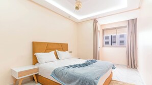 A bedroom with a bed, nightstand, and a window with curtains. - Clean & Affordable 1BR in Agadir  24/7 Staff (Agadir)