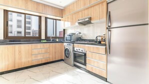 A modern kitchen with wooden cabinets, a stainless steel refrigerator, a washing machine, and a microwave. - Clean & Affordable 1BR in Agadir  24/7 Staff (Agadir)