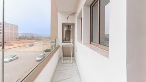 A narrow balcony with a glass railing, a small table, and a view of a construction site. - Clean & Affordable 1BR in Agadir  24/7 Staff (Agadir)