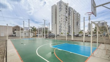 An outdoor basketball court with a net, surrounded by a fence, and adjacent to a multi-story residential building.