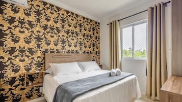 A bedroom with a bed, a nightstand, a window with curtains, and a wall with a patterned wallpaper.