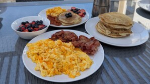 En morgenmadstallerken med pandekager, røræg, bacon og frugt.