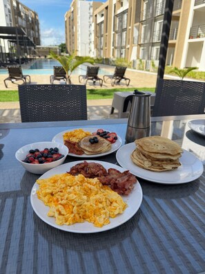 A breakfast table with pancakes, scrambled eggs, bacon, and fruit. - Your relaxation 15 minutes away from the airport, port and beaches (Punta Cana)