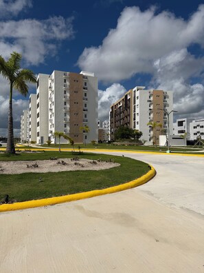 A modern residential complex with multiple high-rise buildings, a well-maintained lawn, and a curved road with a yellow curb. - Your relaxation 15 minutes away from the airport, port and beaches (Punta Cana)