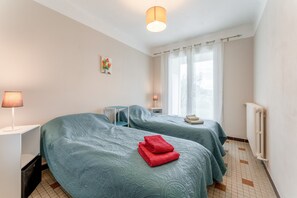 Een hotelkamer met twee bedden, een tafeltje, een lamp en een radiator.