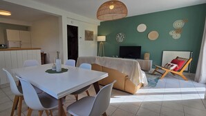 En moderne stue med sofa, spisebord med stole, fjernsyn og dekorativ vægkunst.