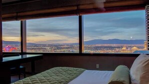 Une chambre d’hôtel dotée d’une grande fenêtre donnant sur le paysage urbain, d’un lit recouvert d’une courtepointe matelassée et d’un bureau avec une chaise.