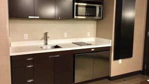 Une cuisine moderne avec des meubles de rangement aux couleurs sombres, un four à micro-ondes en acier inoxydable, un évier et un lave-vaisselle.