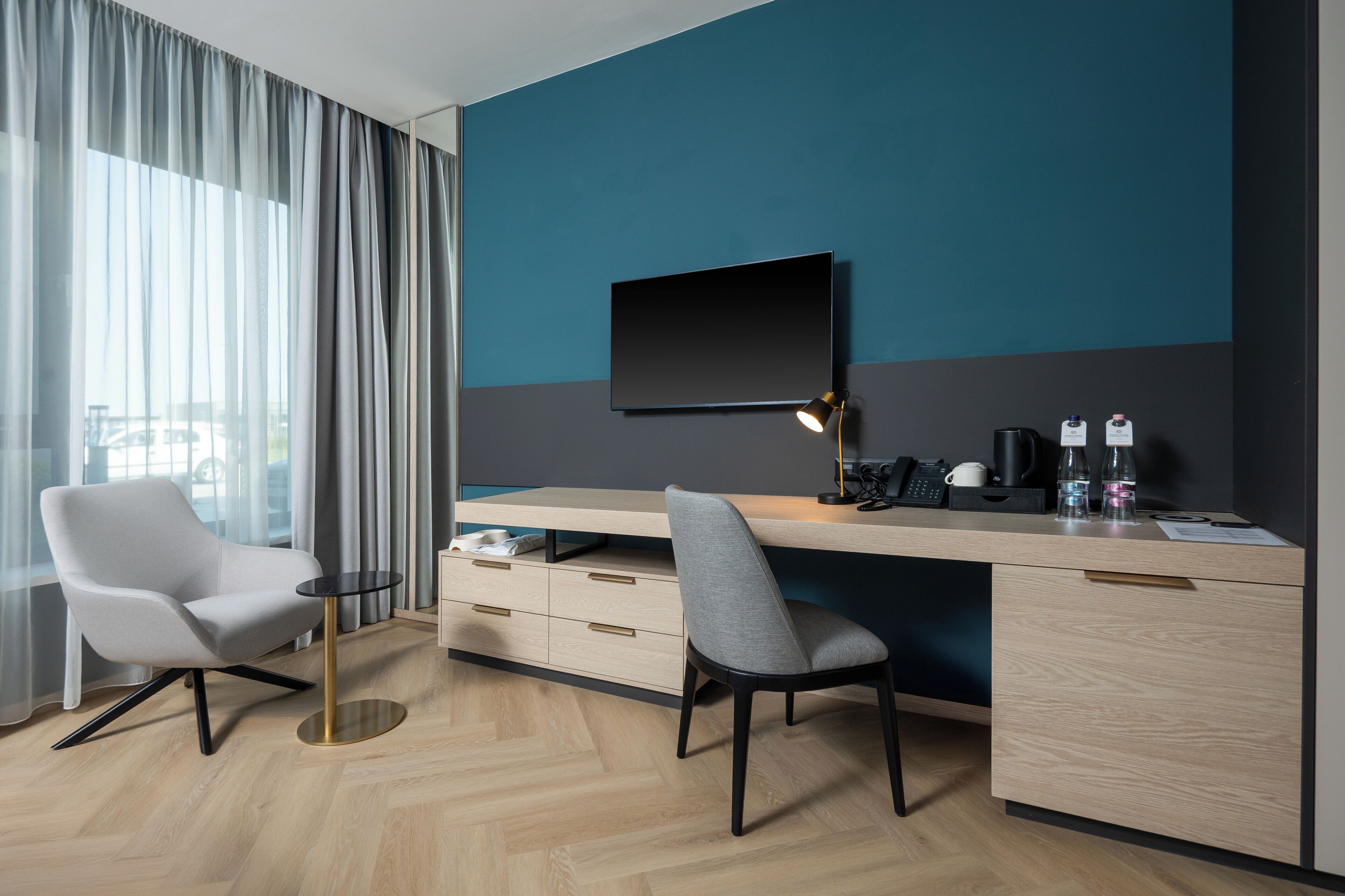 A modern hotel room with a desk, two chairs, a TV, and a coffee maker.
