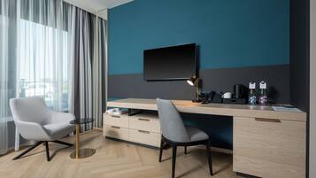 Una habitación de hotel moderna con escritorio, dos sillas, televisión y cafetera.