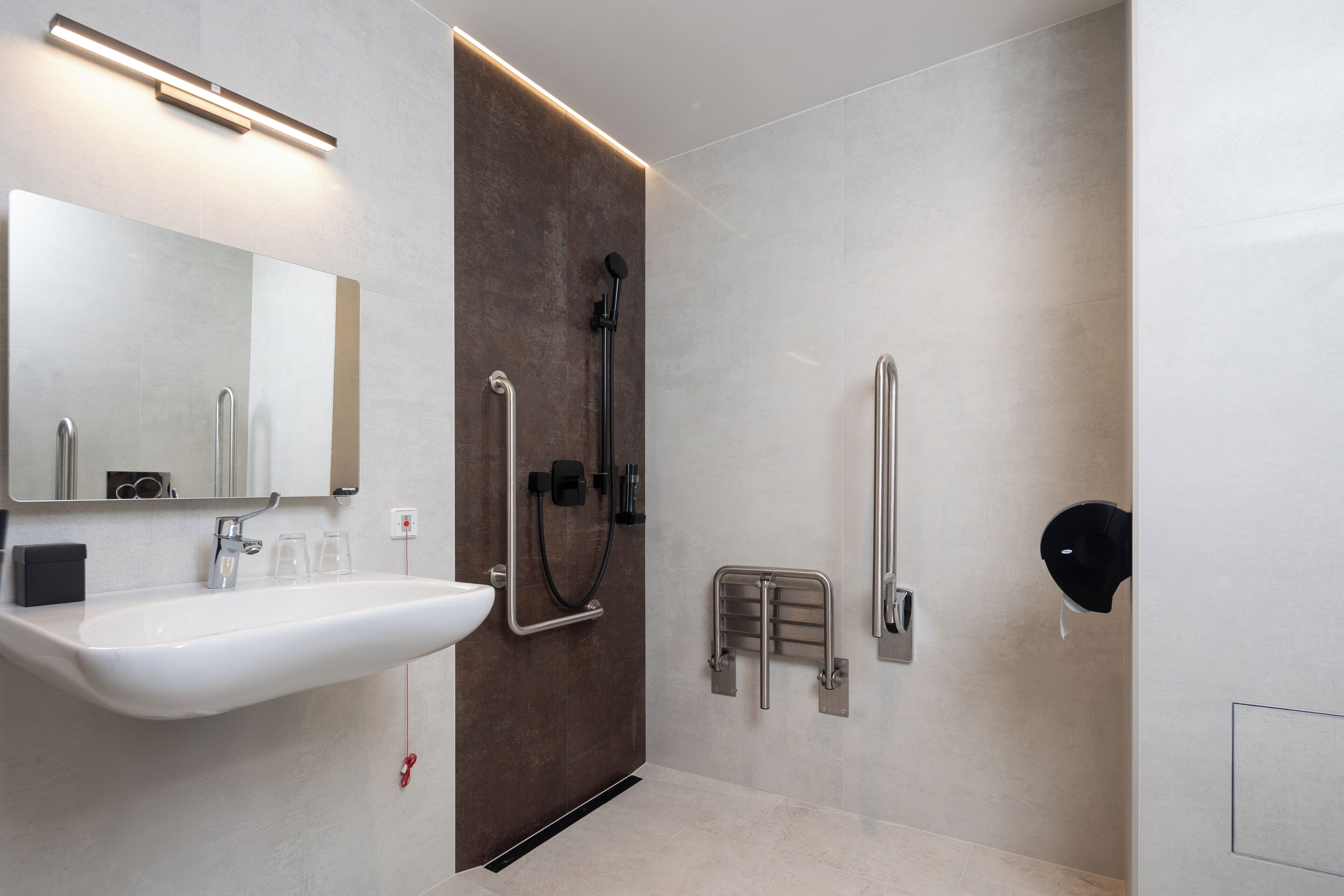 Un baño moderno con un lavamanos blanco, un espejo, una ducha con cabezal de ducha manual y una barandilla.