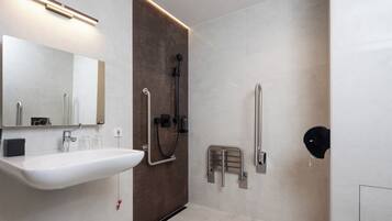 Un baño moderno con un lavamanos blanco, un espejo, una ducha con cabezal de ducha manual y una barandilla.