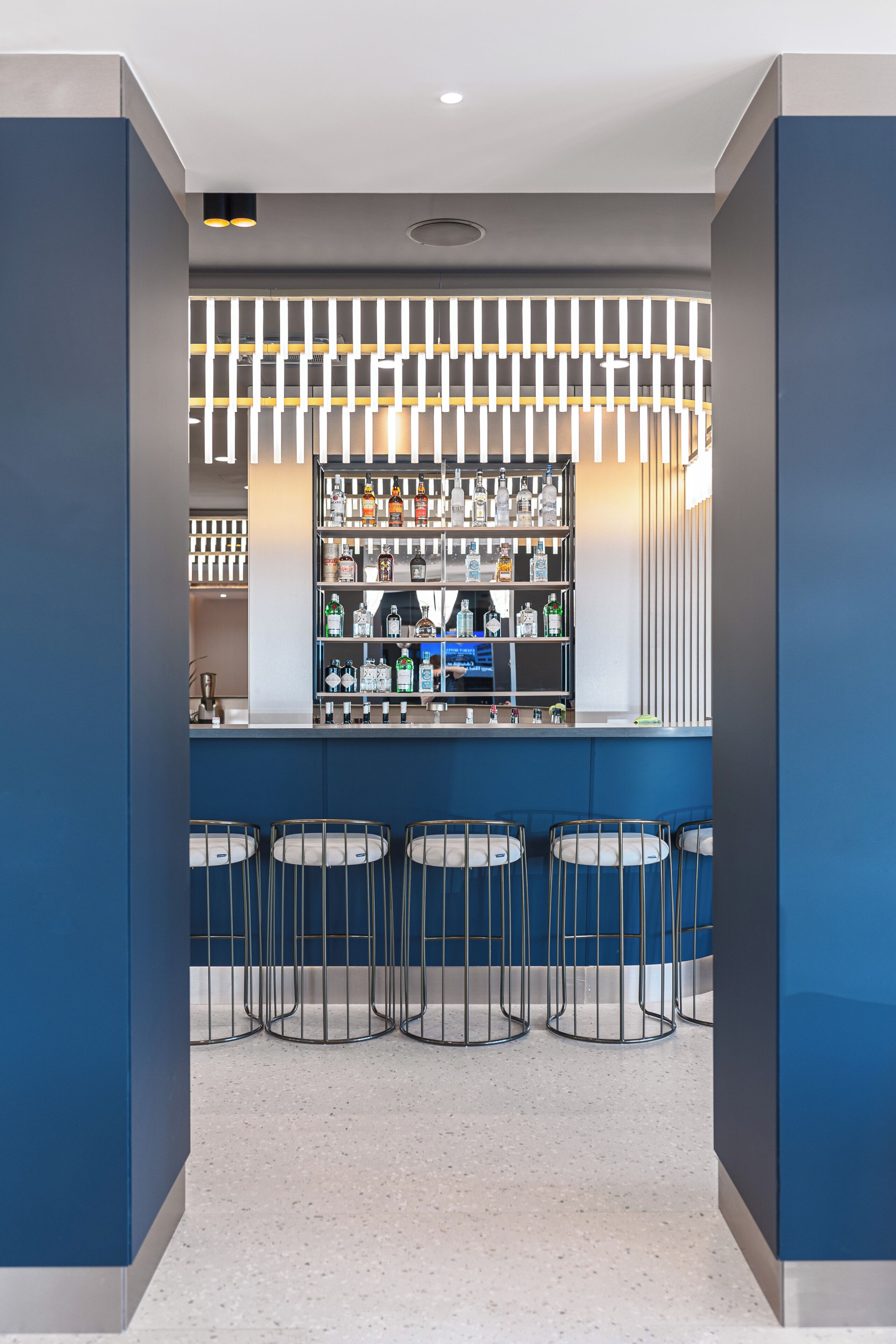 Zona de bar con diseño moderno, que incluye una barra, varios estantes con botellas y tres taburetes.