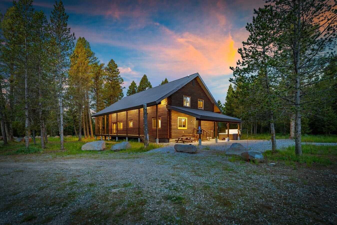 A log cabin with a porch, surrounded by trees, and a gravel driveway.