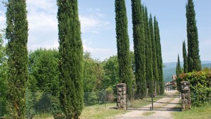 A pathway leading to a gated area with tall cypress trees and a stone structure. - Casa Fantone. Villa with private pool and large fenced park for absolute privacy (Poppi)