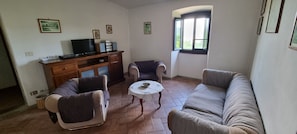 A living room with a sofa, two armchairs, a coffee table, a TV on a wooden cabinet, and a window with a view. - Casa Fantone. Villa with private pool and large fenced park for absolute privacy (Poppi)