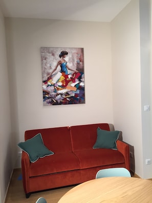 Una habitación con un sofá rojo, dos almohadas verdes y un cuadro en la pared.