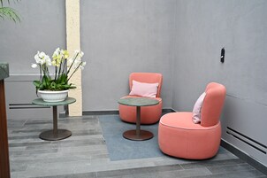 Un interno moderno con due poltrone rosa, un tavolino e una pianta in vaso con fiori bianchi.
