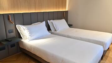 Una camera d'albergo con due letti singoli, una testiera in legno, comodini e un tavolino con un telecomando.
