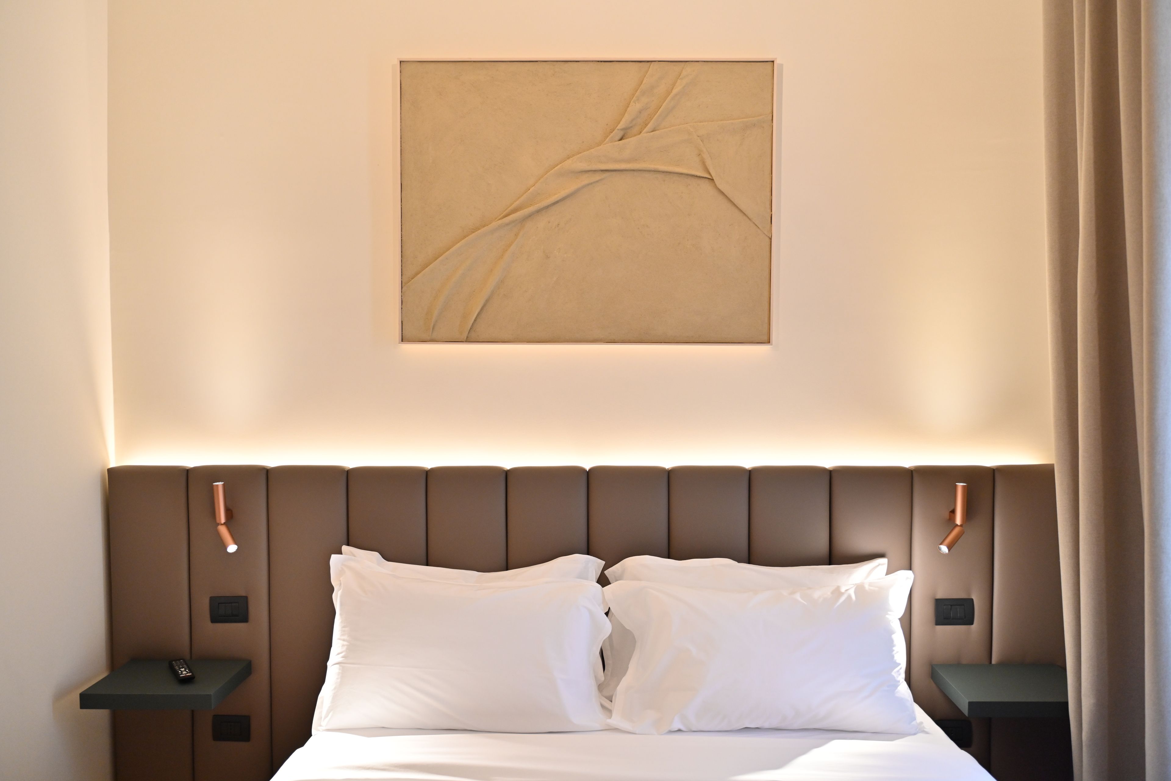 Una habitación de hotel con cama, dos mesitas de noche, un cuadro colgado en la pared y una cortina.