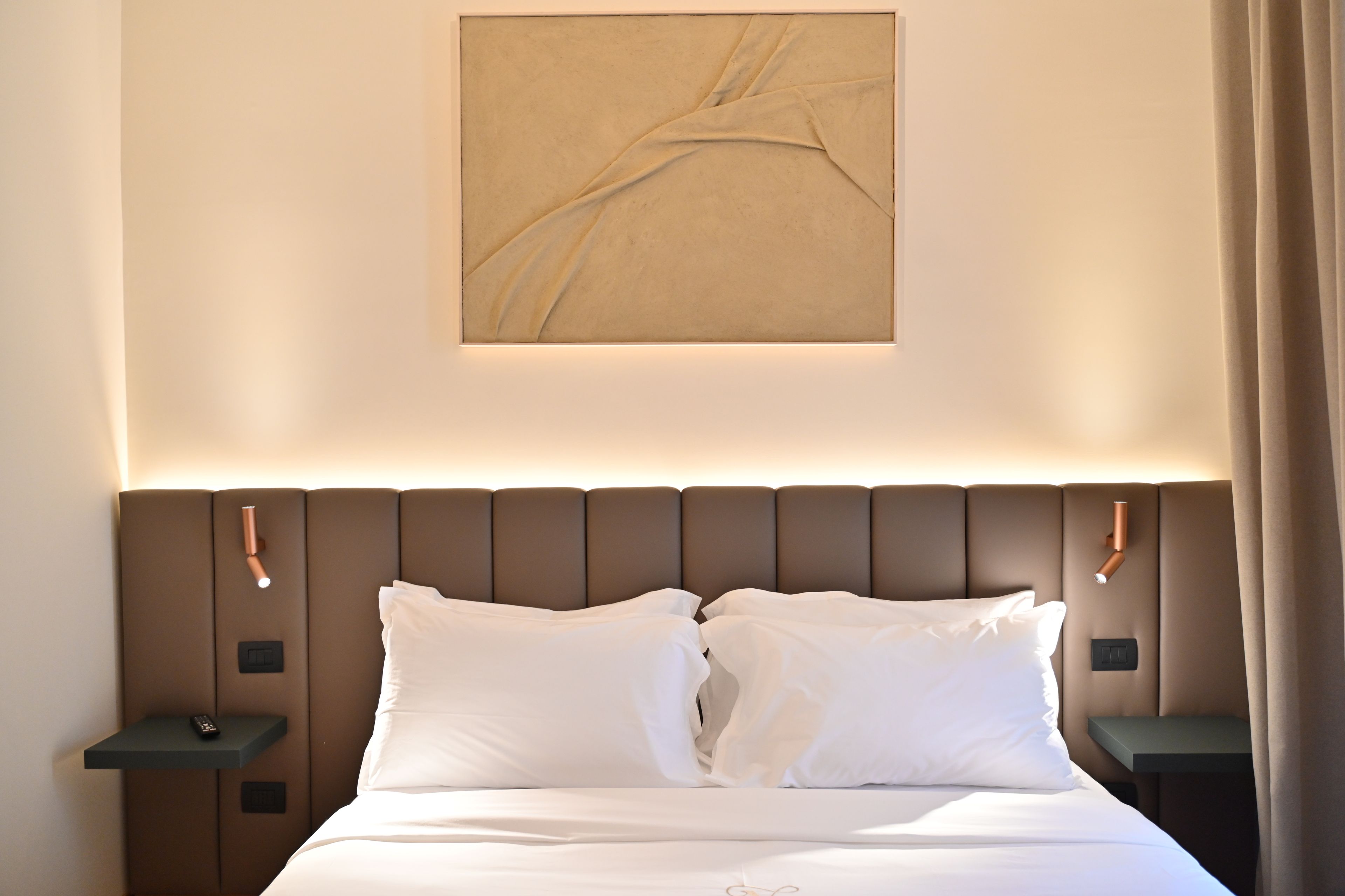 A hotel room with a bed, two bedside tables, a wall-mounted artwork, and a curtain.