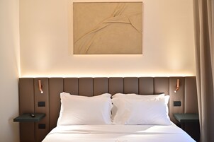 Una habitación de hotel con una cama, dos mesitas de noche, una obra de arte en la pared y una cortina.
